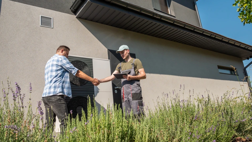 Photographie d'un technicien climat ou du responsable de Thermo-Logis souriant et bienveillant, discutant face à face avec un client dans l'intérieur résidentiel de celui-ci, à proximité d'une unité Mitsubishi Electric installée. L'atmosphère doit transmettre la confiance, la disponibilité et l'écoute attentive. Éviter les poses figées ou génériques : privilégier un moment authentique de dialogue professionnel et courtois reflétant la relation de proximité et la personnalisation du service.